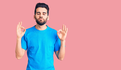 Fototapeta premium Young handsome man with beard wearing casual t-shirt relaxed and smiling with eyes closed doing meditation gesture with fingers. yoga concept.