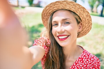 Young blonde woman on vacation smiling happy making selfie by the camera sitting on the park