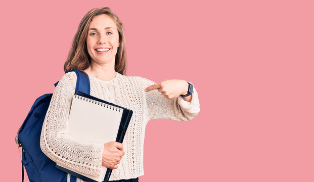 Young beautiful blonde woman wearing student backpack holding notebook pointing finger to one self smiling happy and proud