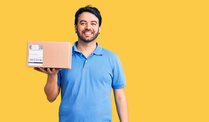 Young hispanic man holding delivery package looking positive and happy standing and smiling with a confident smile showing teeth
