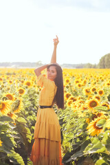 A brunette woman in a yellow dress on the field with sunflowers. Orange dress.