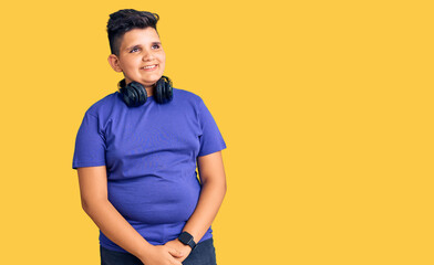 Little boy kid listening to music wearing headphones looking away to side with smile on face, natural expression. laughing confident.