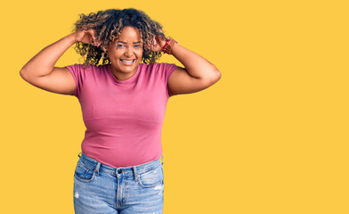 Young african american plus size woman wearing casual clothes smiling pulling ears with fingers,...