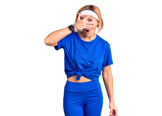 Fototapeta premium Young blonde woman wearing sportswear peeking in shock covering face and eyes with hand, looking through fingers with embarrassed expression.
