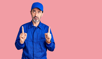 Fototapeta premium Middle age handsome man wearing mechanic uniform pointing up looking sad and upset, indicating direction with fingers, unhappy and depressed.