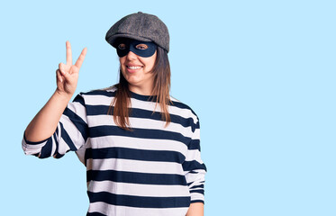 Young beautiful brunette woman wearing burglar mask smiling with happy face winking at the camera...