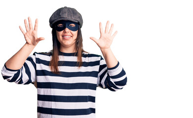 Young beautiful brunette woman wearing burglar mask showing and pointing up with fingers number ten while smiling confident and happy.