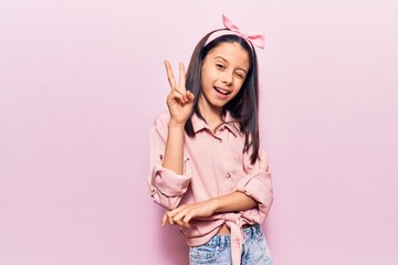 Beautiful child girl wearing casual clothes smiling with happy face winking at the camera doing victory sign with fingers. number two.