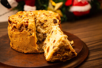 Fruit panettone covered with chestnuts on wooden board, with slice, on a table decorated for Christmas