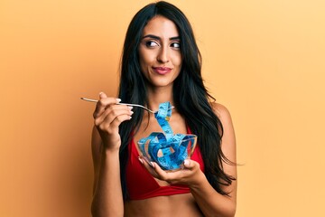 Beautiful hispanic woman eating measure meter doing diet for weight loss smiling looking to the...