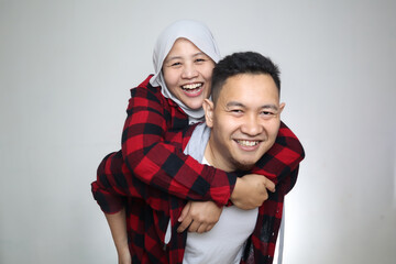 Happy Asian muslim couple posing to camera, man carry his wife on his back, piggyback, smiling...