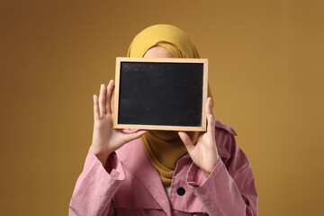 Muslim woman wearing hijab covering her face with blackboard, anonymouse facial expression
