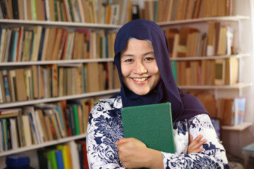 Asian muslim woman wearing hijab reading book in library, educational. Happy smiling expression when doing leisure activity