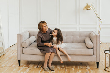 Family concept. Grandmother and granddaughter are sitting on the sofa in a light interior.