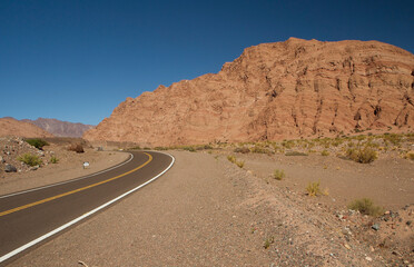 Road trip. Traveling along the asphalt route across the arid desert and valley. The empty highway, sand, sandstone and rocky hills under a deep blue sky.