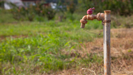 Selective focus with blurred background of grunge and rusty faucet installed in the field of remote rural area for people living and agriculture shows problem of water shortage and global warming