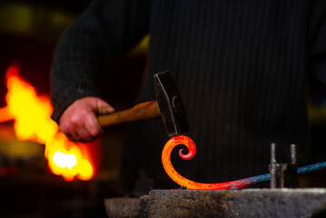 A blacksmith forging a curl from a red-hot flattened billet with a hammer. Handmade in the forge concept