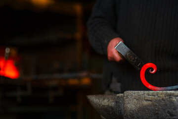 A close-up image of a blacksmith's hands forging a spiral from a red-hot billet against the...