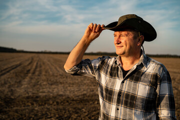 Farmer holding edge of hat, while he looks toward his field