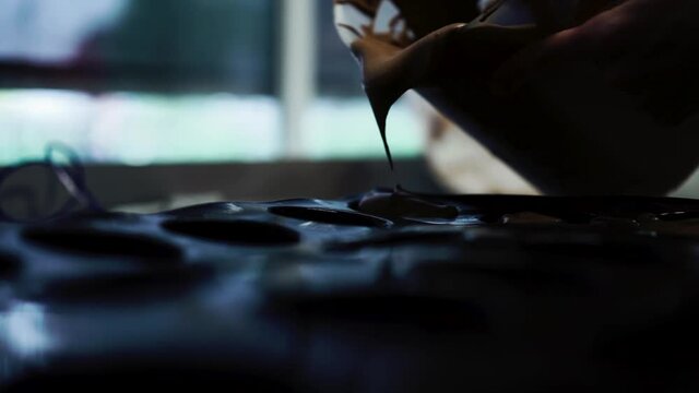 Extreme close up shot of baker dropping chocolate mix into cupcake tray in slow motion