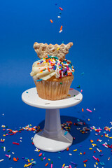 Cannoli Cupcake on White Pedestal with Sprinkles on Blue Background