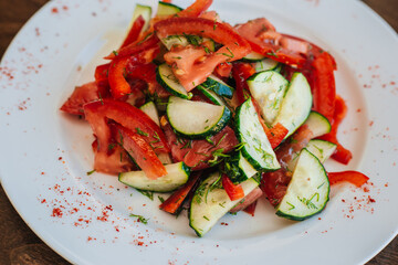 Classic salad with cucumbers and tomatoes sprinkled with dill. Diet food. On a white plate. Dish on a dark background.
