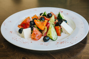 Diet salad. Tomatoes with cucumbers and olives, cubes of white soap and a cabbage leaf. Healthy food, white dish on a dark background