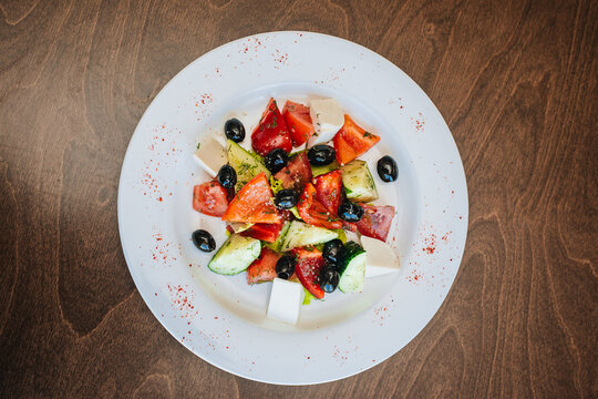 Diet Salad. Tomatoes With Cucumbers And Olives, Cubes Of White Soap And A Cabbage Leaf. Healthy Food, White Dish On A Dark Background