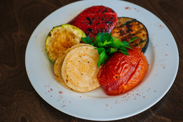 Baked vegetables. Grilled eggplants with tomatoes and zucchini. Vegetarian food. White dish on a dark background