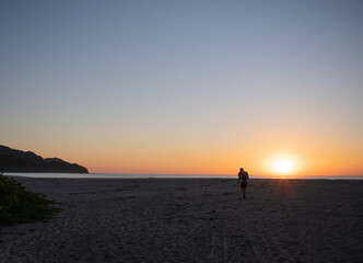 man walking in the sunset on a beautiful beach with a blue sky