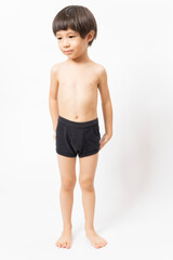 Cute little Asian 3 years old toddler boy wearing black shorts standing on white background.