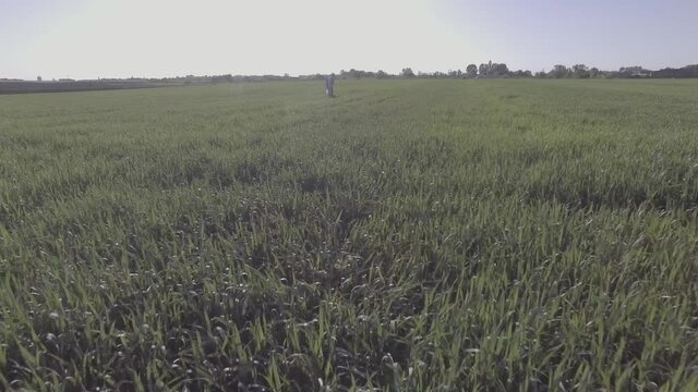 View from the back. The camera flies away from a praying person who is standing in the middle of a green field. He is wearing tefillin and tallit. The camera moves to the left around him