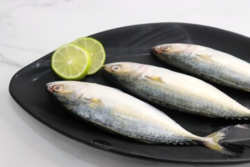 Uncooked Indian mackerel fish Rastrelliger kanagurta. also known as Bangda fish. Free copy space. Lemon wedge and coriander. top view fish background. online fish marketing. 
