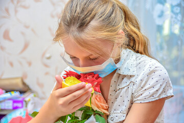 A girl in a protective mask holds a bouquet of flowers and sniffs roses, quarantined for the duration of the covid-19 virus pandemic.