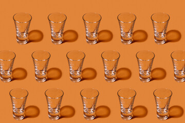 Abstract pattern. Repetition of empty liquor glasses on orange background. Textured background of glass glasses standing in a row. Abstract geometric orange background. Art photo concept.