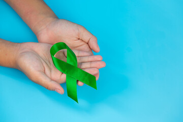 World Mental Health Day; green ribbon put in human's hands on blue background