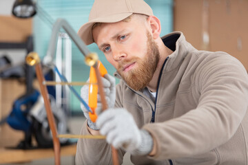 tradesman cutting copper pipe with hacksaw