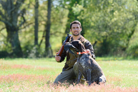 hunter kneeled by his dog gun slung over shoulder