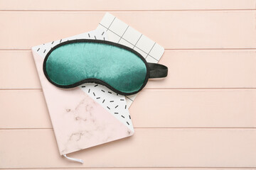 Sleeping mask and notebooks on wooden background