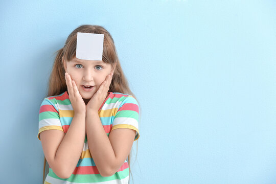 Surprised little girl with blank note paper on her forehead against color background