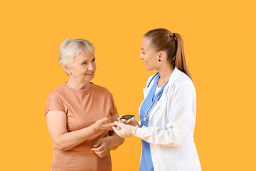 Doctor checking blood sugar level of senior diabetic woman on color background