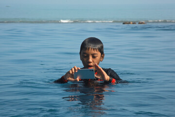 Asian boy using smartphone in the swimming pool. Technology, summer and holiday concept