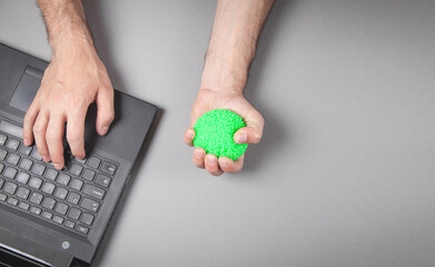 Obraz premium Man squeezing stress ball while working with laptop.