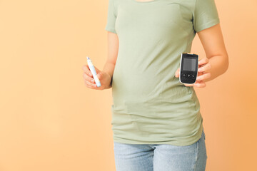 Pregnant diabetic woman with digital glucometer and lancet pen on color background