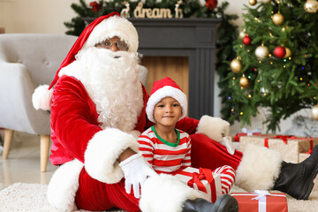 Fototapeta na wymiar African-American Santa Claus and cute boy with gifts at home on Christmas eve
