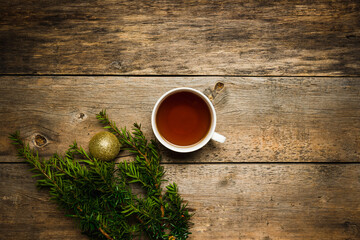 Christmas hygge background with cup of tea, pine branches and christmas ball on the wooden background. Selective focus. Shallow depth of field. 
