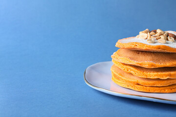 Plate with tasty pumpkin pancakes on color background