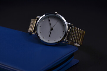 Women's watch is on the notebook. Dark background.