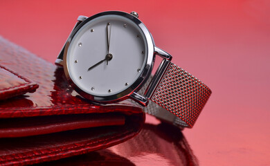 A wrist watch and a wallet lie on a red background.
