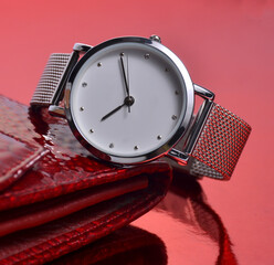 Women's watch and wallet lie on a red background.